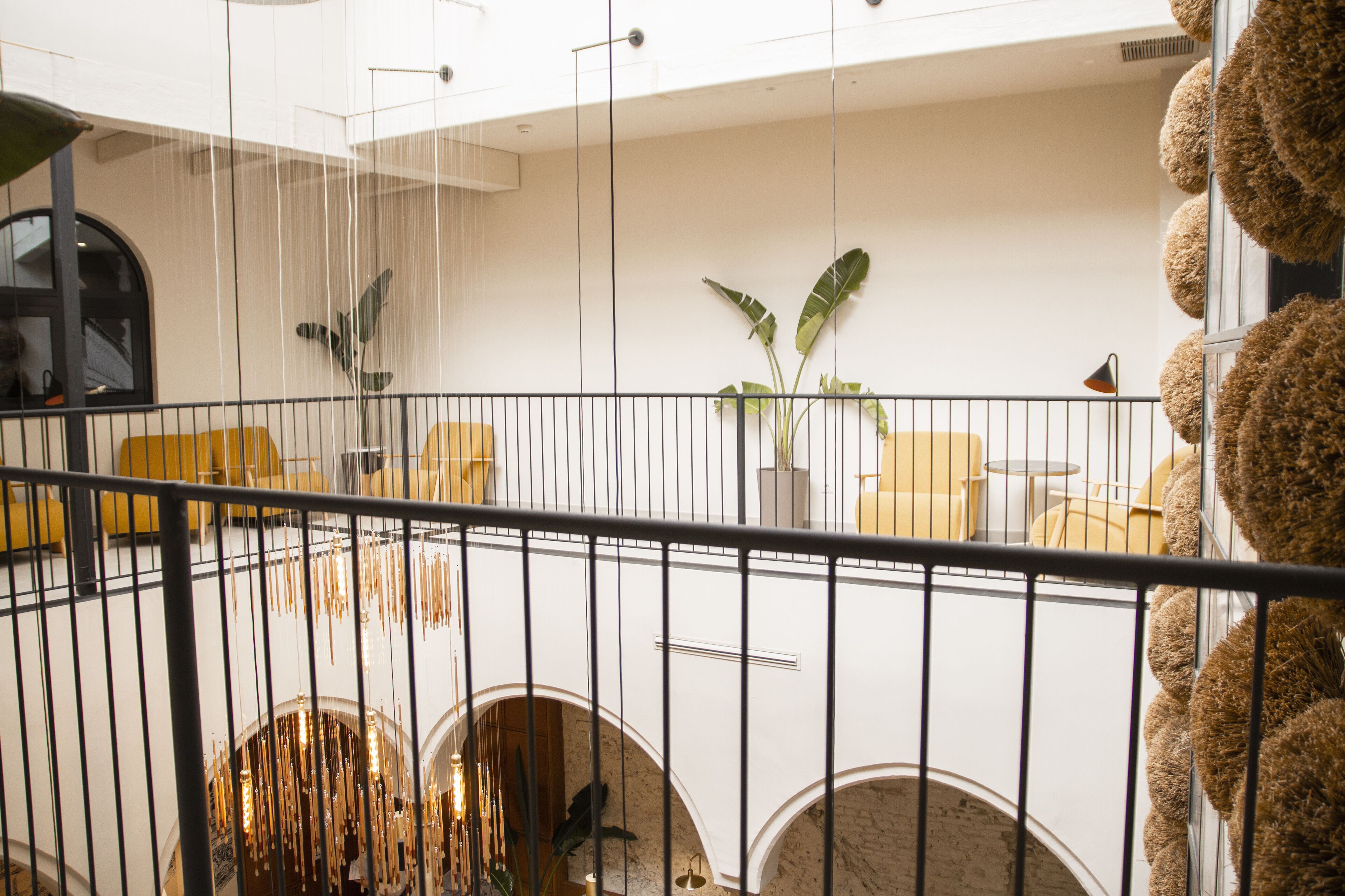 Un intérieur moderne avec un plafond haut, une plante au centre et un coin salon avec des chaises jaunes.