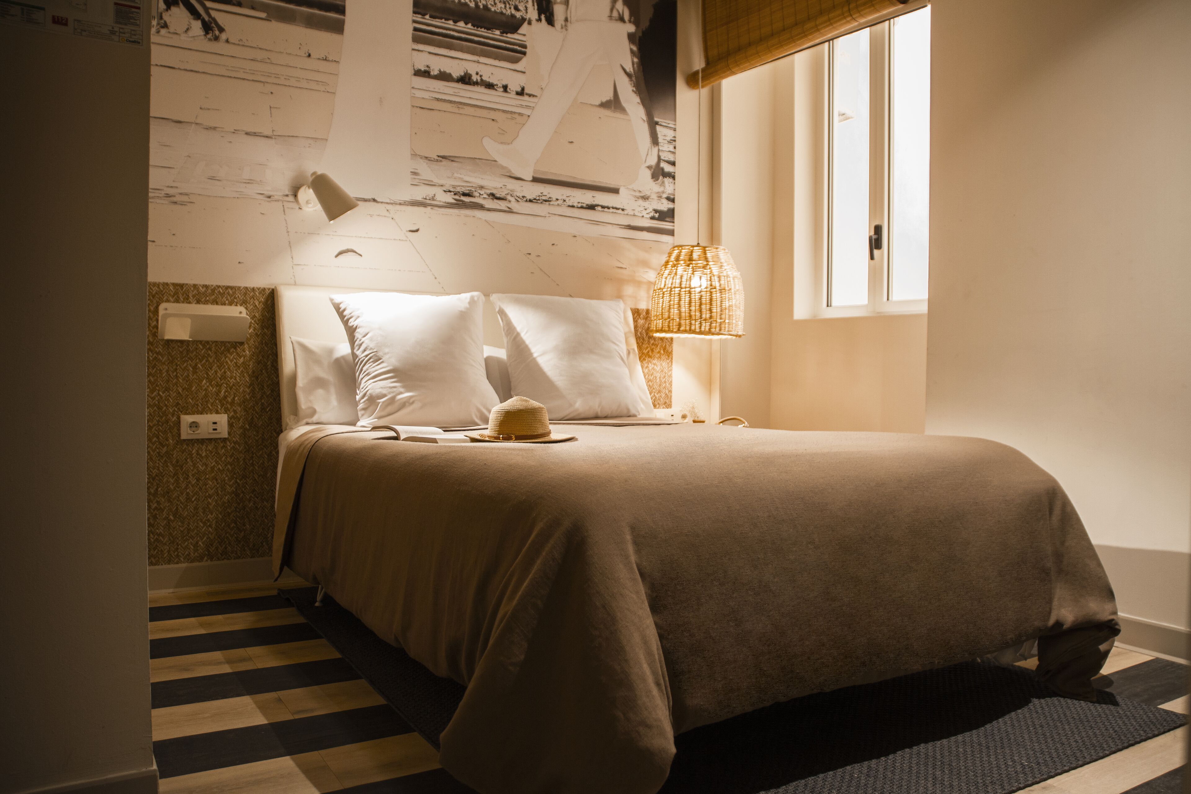 Una cama bien hecha con cabecera, una lámpara de noche y una ventana con vistas al exterior.