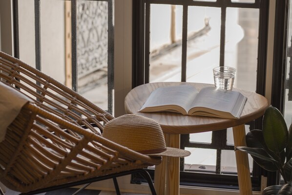 A wicker chair, a small round table with an open book and a glass of water, and a window with a view of a snowy street.