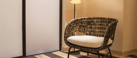 Une pièce avec un sol à rayures, une chaise en osier dotée d’un coussin et deux lampes en osier suspendues au plafond.