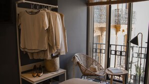 A bedroom with a bed, a chair, a small table, a window with a view, and a clothing rack with hanging clothes. - Select Tetuán (Seville)