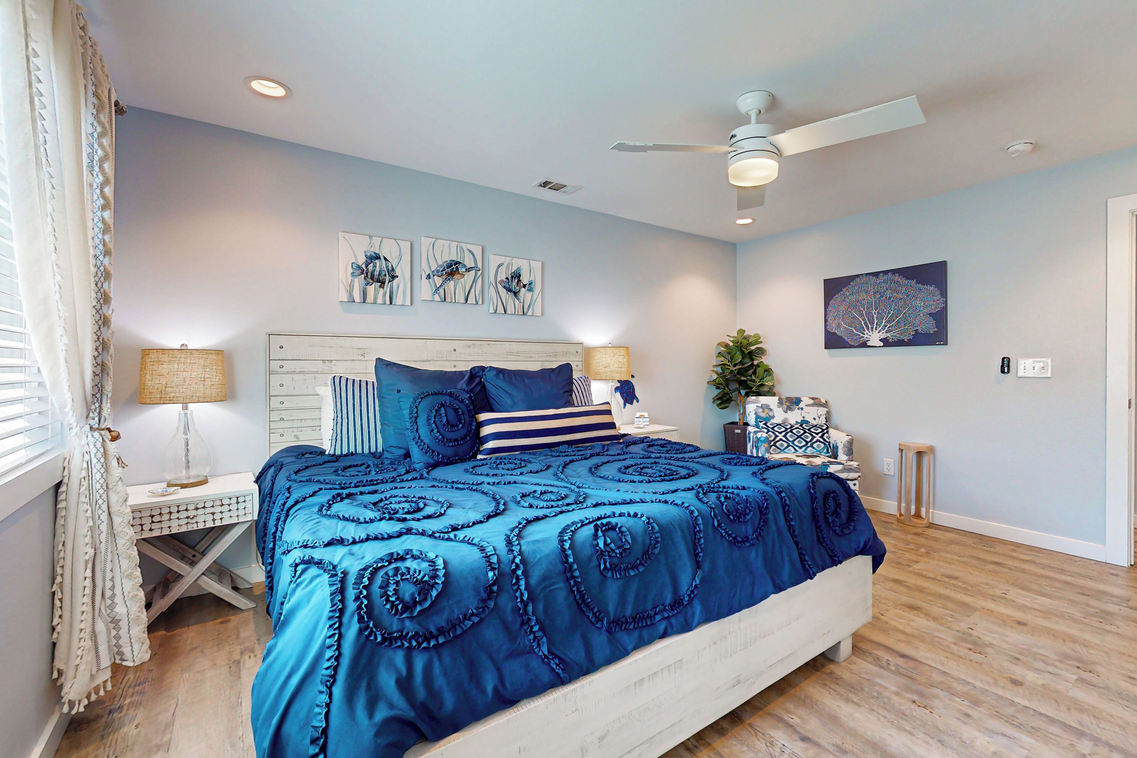 A bedroom with a bed, bedside tables, a ceiling fan, and wall art.