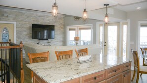 A kitchen with a large island, wooden chairs, a television mounted on the wall, and pendant lights. - Herring House- Gulf front, St Joe Beach, WIFI, No pets, Sleeps 7 (Saint Joe Beach)