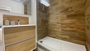 A modern bathroom with a glass-enclosed shower, wooden wall tiles, and a white vanity with a mirror. - Le Cocon / Hyper-Centre / Air-conditioning / Trams (Grenoble)