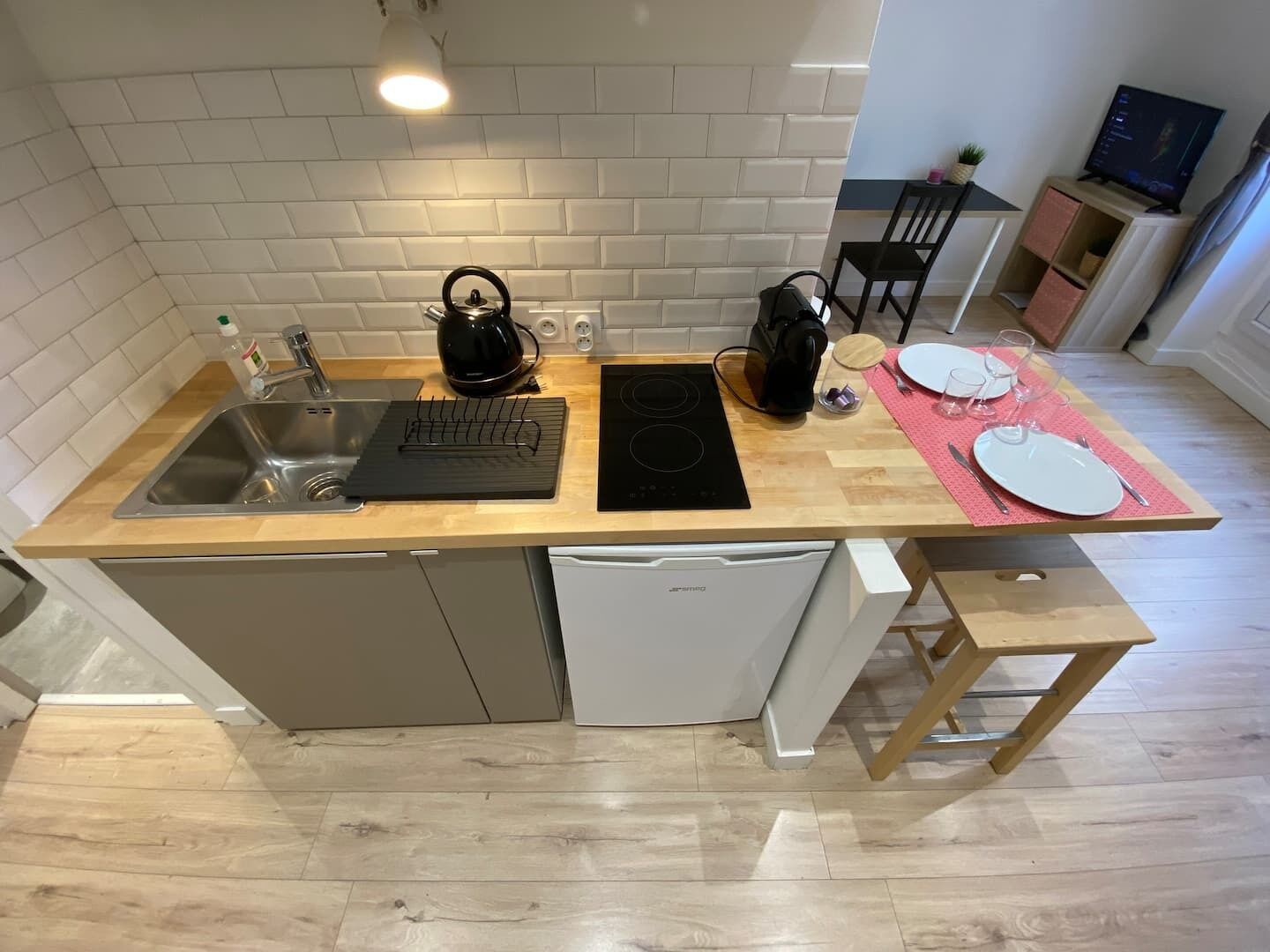 Une cuisine compacte équipée d’un évier, d’une bouilloire, d’une plaque de cuisson à induction et d’un petit coin repas avec une table et des chaises.