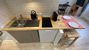 Une cuisine compacte équipée d’un évier, d’une bouilloire, d’une plaque de cuisson à induction et d’un petit coin repas avec une table et des chaises.
