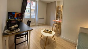 A compact living space with a dining area, a small round table, a TV on a stand, and a window with a view of buildings. - Le Cocon / Hyper-Centre / Air-conditioning / Trams (Grenoble)