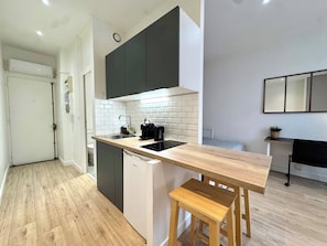 Una cocina moderna con encimera de madera, electrodomésticos integrados y un taburete pequeño.