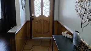 Un couloir avec une porte en bois, une pancarte de bienvenue, un vase décoratif et une œuvre d’art accrochée au mur.