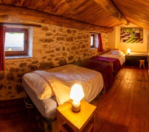 A rustic room with stone walls, wooden floors, two beds with red bedding, a nightstand with a lamp, and a window with red curtains. - 3 Bedroom Agritourism property in SABRAN (SABRAN)