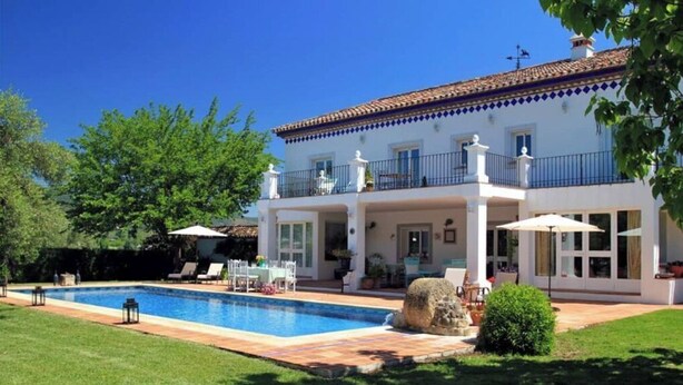 Una casa de dos pisos con piscina, mobiliario exterior y un jardín bien cuidado.