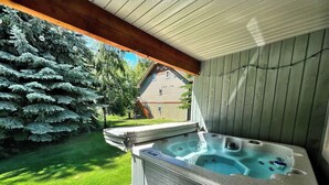 Un jacuzzi bajo una pérgola de madera con vistas a una casa y un gran abeto.