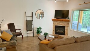 A living room with a fireplace, a television, a sofa, a chair, and a coffee table. - Willow Vistas 6 - Golf - Ski - Hike - Chill - Private Hot Tub - Sleeps 6 (Kimberley)