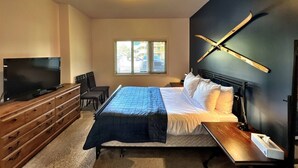 Un dormitorio con una cama, televisión, escritorio y ventana.