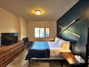 A bedroom with a bed, a TV, a desk, and a window.
