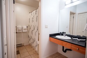 Une salle de bain avec un lavabo blanc, un miroir et un rideau de douche orné d’un motif de feuilles.