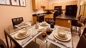 Una cocina moderna con armarios de madera, un refrigerador negro y un comedor con platos y vasos blancos.
