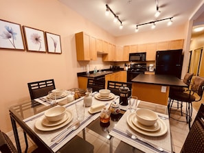 A modern kitchen with wooden cabinets, a black refrigerator, and a dining area set with white plates and glasses.