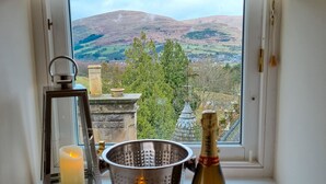 Une fenêtre donnant sur un paysage montagneux, une bougie, une passoire en métal et une bouteille de champagne.