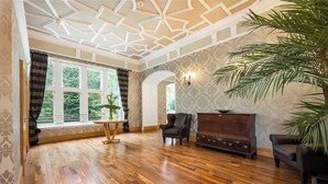 Une pièce spacieuse avec un plancher en bois, une grande fenêtre avec des rideaux, une plante et un meuble en bois foncé.
