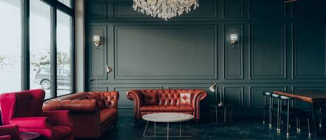 A modern lounge with a leather sofa, red chairs, a round coffee table, and a chandelier.
