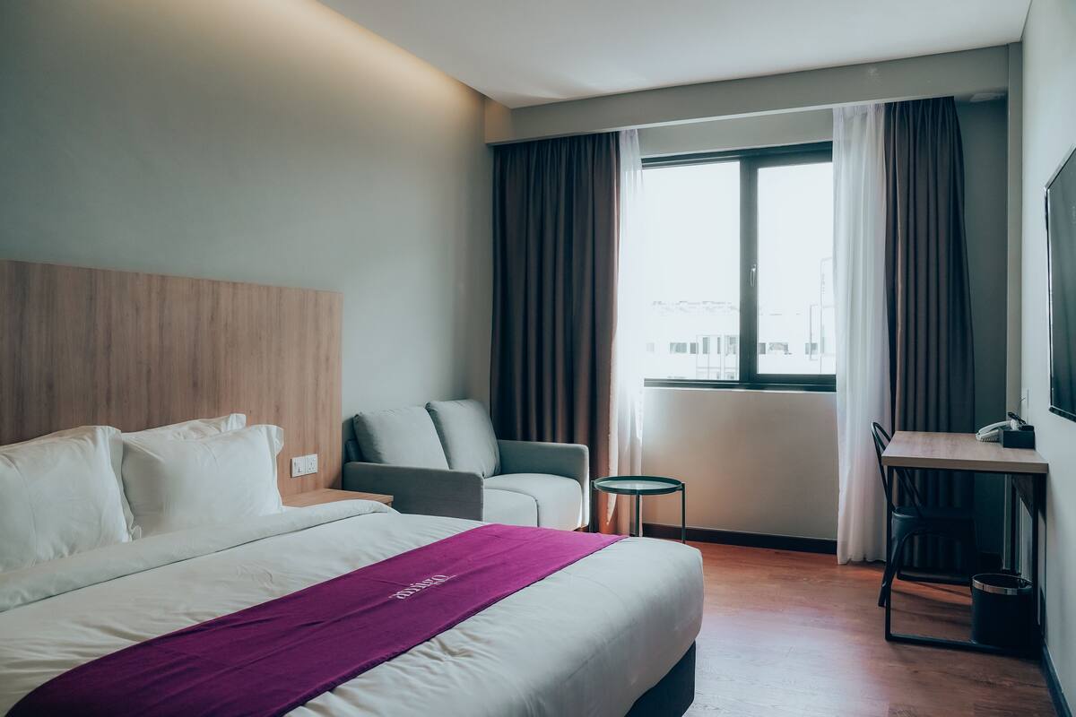 Une chambre d’hôtel avec un lit, un bureau, une chaise et une fenêtre avec des rideaux.