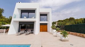 Et moderne hus med to etager, en swimmingpool, udendørs møbler og en velplejet have.