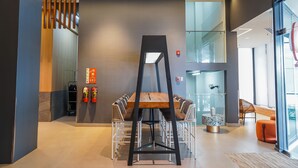 A modern dining area with a wooden table and white chairs, a glass partition, and a fire extinguisher on the wall. - Go Hotels Plus Naga (Naga)