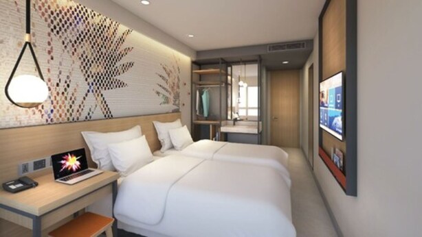 A hotel room with two beds, a desk with a laptop, a wall-mounted TV, and a decorative wall panel. - Go Hotels Plus Naga (Naga)