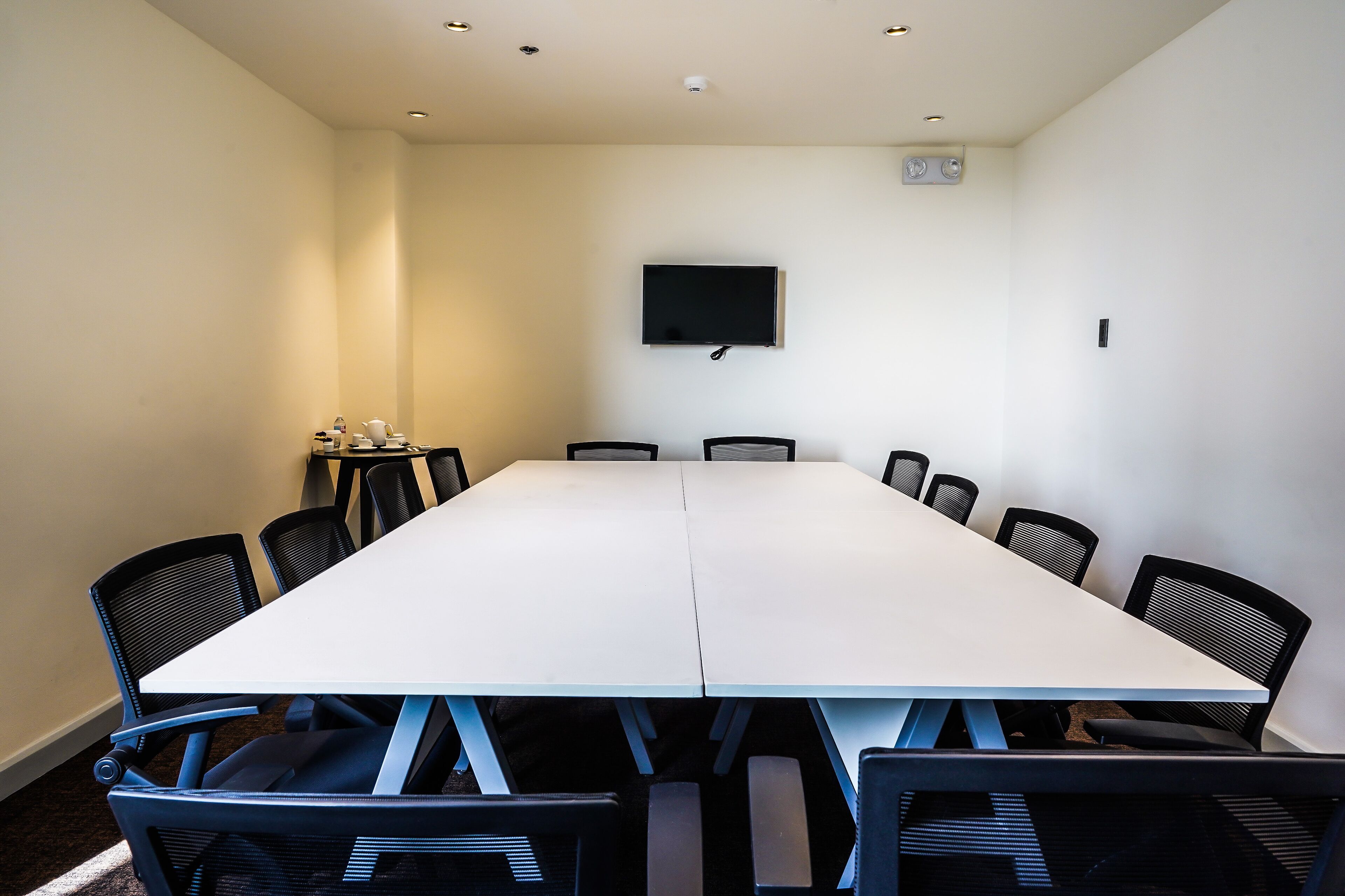 A conference room with a long table, black chairs, a flat-screen TV, and a small table with cups and a teapot.