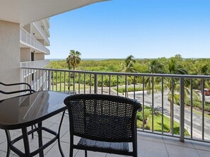 A balcony with a table and chairs, overlooking a road and greenery.