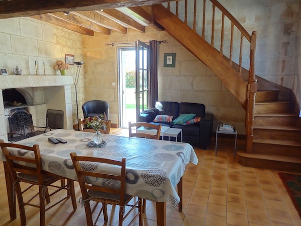 A rustic interior with a dining area, a fireplace, a sofa, and a wooden staircase.