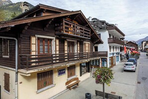 A traditional wooden building with a balcony, a bench, and a flower pot on the sidewalk.