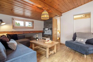 Una sala de estar acogedora con techo de madera, pared de piedra, mesa de madera con una botella y vasos, y un televisor.