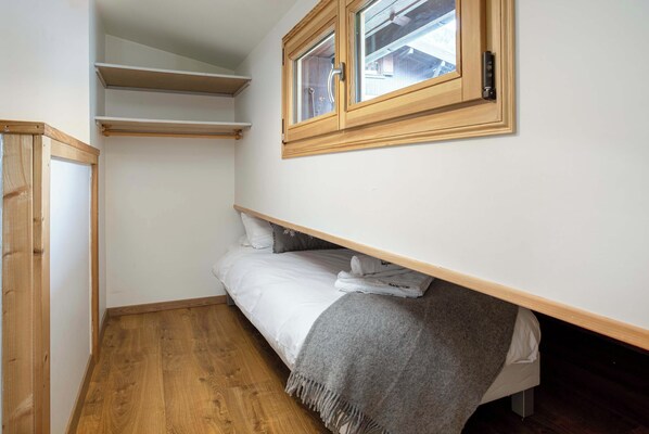 A small bedroom with a bed, a wooden wardrobe, a window, and a built-in shelf.