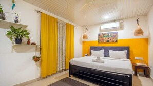 Un dormitorio con cama, cortina amarilla, aire acondicionado instalado en la pared y un cuadro.