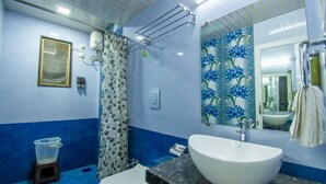 Un baño con un lavamanos blanco, una ducha con cortina estampada y una pared con azulejos azules y blancos.