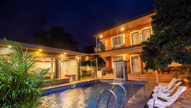 Un área de piscina con un edificio de dos pisos, un espacio de estar cubierto y una escalera que conduce al nivel superior.