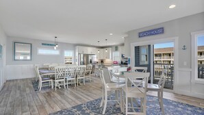 A spacious kitchen with white cabinets, a dining area with white chairs, and a sign reading 'BEACH HOUSE'. - Rushin to the Beach: Spacious 8-bedroom oceanview home in Oak Island, perfect for families. (Oak Island)