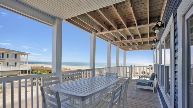 A covered outdoor deck with a table and chairs, overlooking a beach. - Rushin to the Beach: Spacious 8-bedroom oceanview home in Oak Island, perfect for families. (Oak Island)