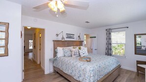 Een slaapkamer met een houten bed, een plafondventilator, een raam met gordijnen en een deur naar een andere kamer.