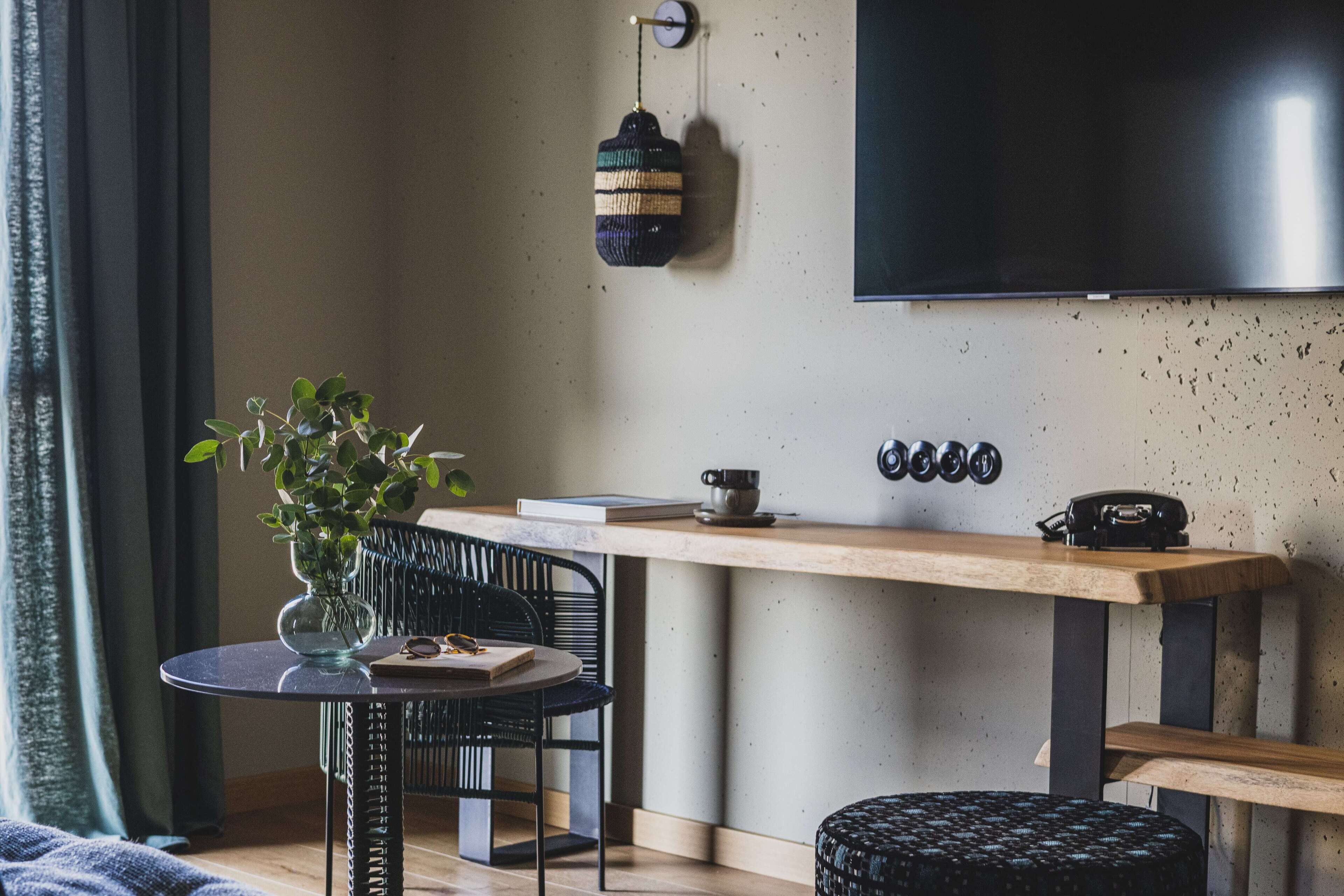 Een moderne woonkamer met een ronde tafel, een zwarte stoel, een kleine potplant, een houten bank en een flatscreen televisie die aan de muur is bevestigd.