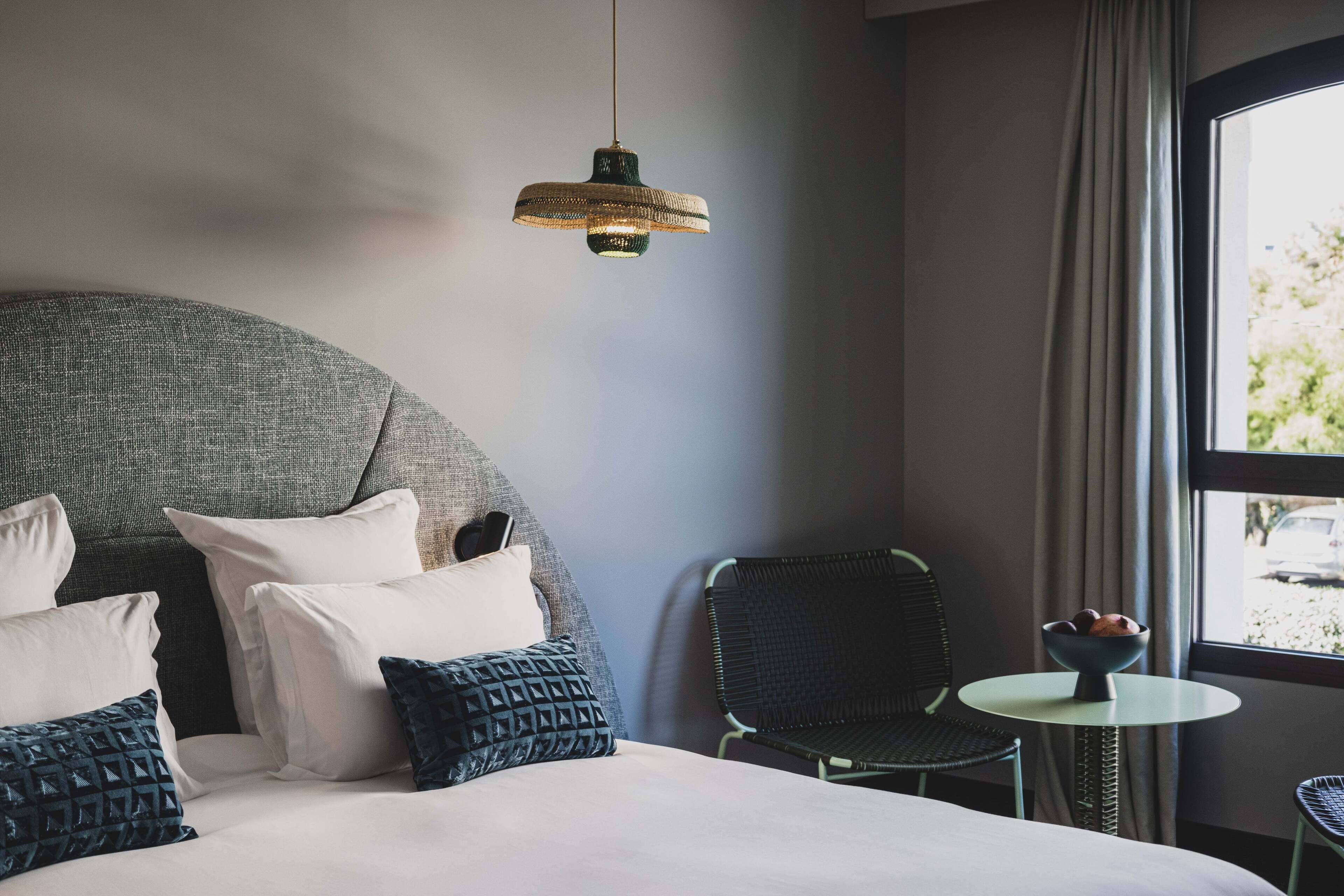 Habitació d'hotel moderna amb un llit gran, una taula rodona petita, una cadira i un penjador de llum.