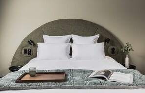 Ein ordentlich bezogenes Bett mit weißen Leinentüchern, ein Tablett mit einem Glas und einem Buch sowie ein Nachttisch mit einer Vase und einer Lampe.