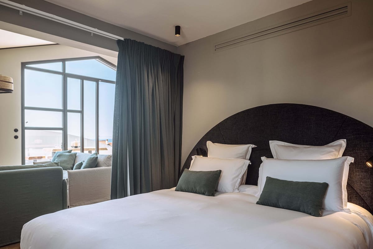 A modern hotel room with a large bed, a curved headboard, and a view of the city through large windows.