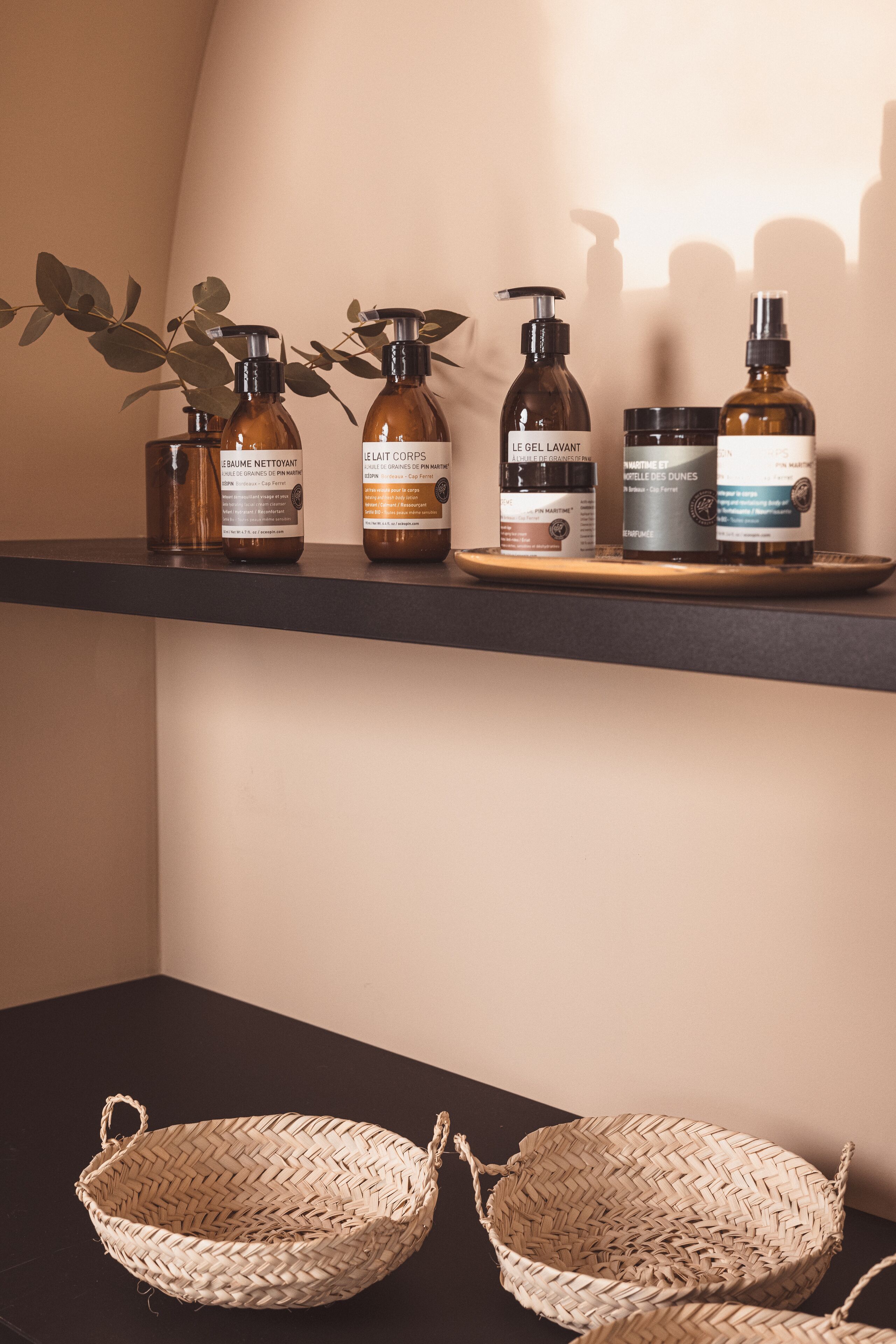 Une étagère avec quatre bouteilles de produits de soins pour le corps et deux paniers en osier posés sur une table.
