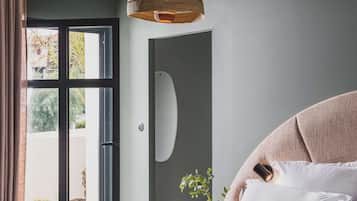 Une chambre avec un grand lit, un luminaire suspendu, une porte-fenêtre coulissante donnant sur un espace extérieur et une petite plante en pot.
