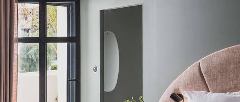 Un dormitorio con una cama grande, una lámpara colgante, una puerta corredera de vidrio que da a un área exterior y una pequeña planta en maceta.