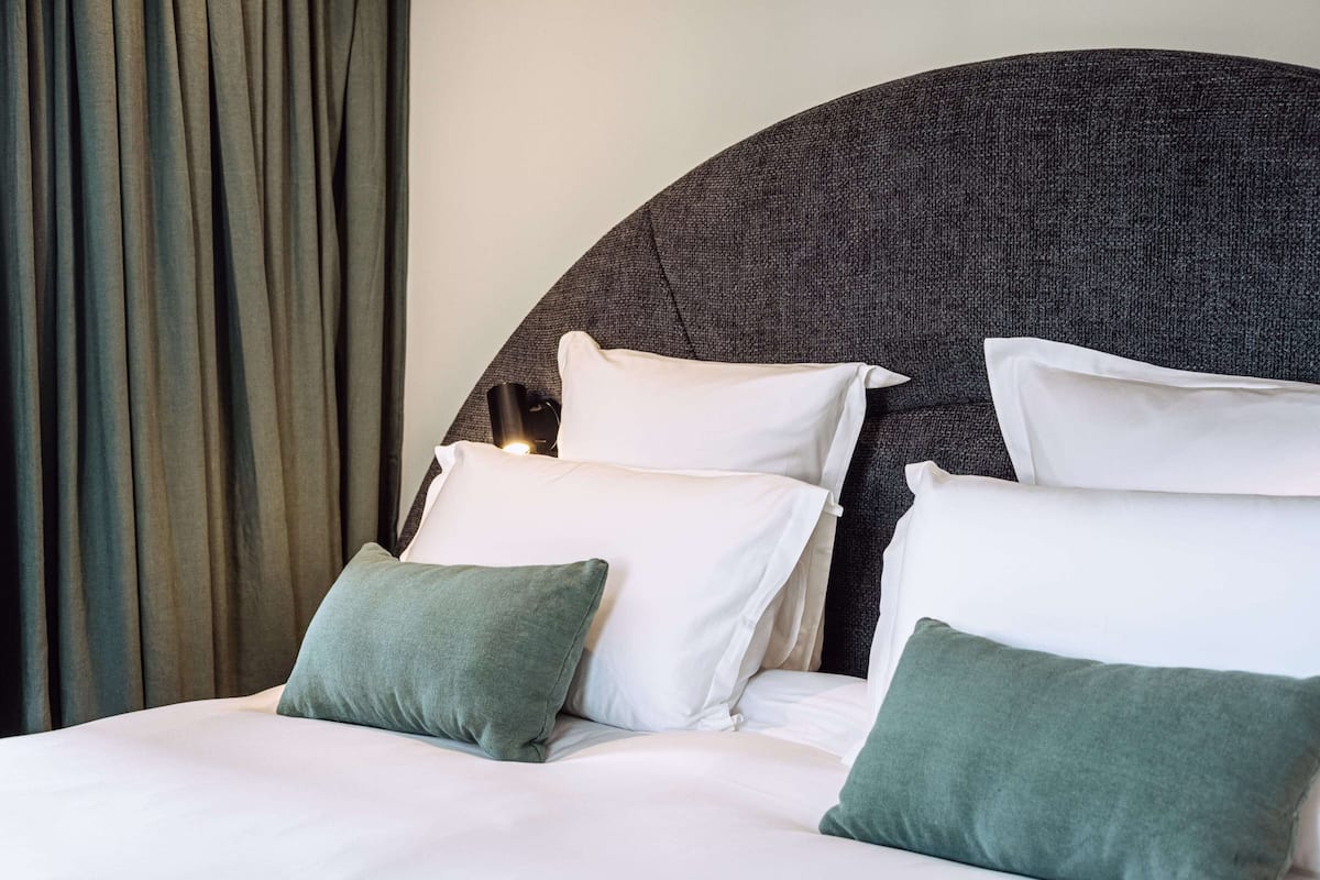 A bed with white and green pillows, a dark headboard, and a curtain in the background.