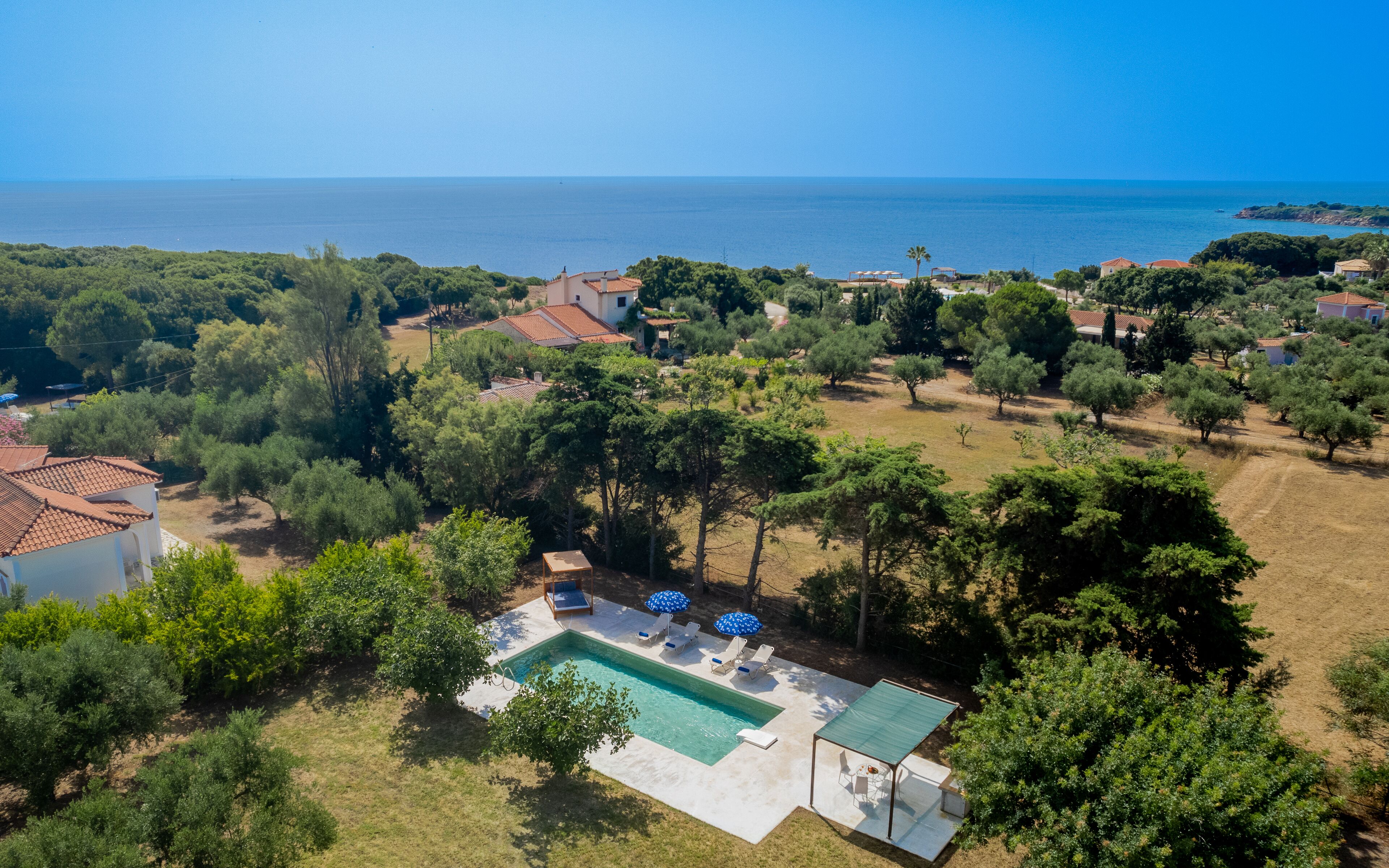 An aerial view of a property with a swimming pool, surrounded by trees and a view of the sea.